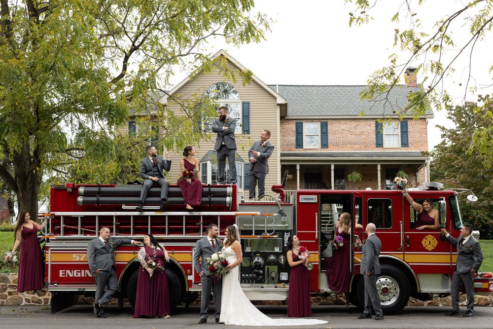 Wedding party poses creatively on and around vintage red fire truck in front of house.