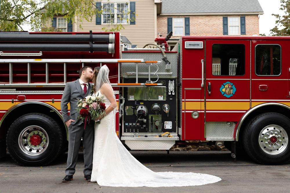 A wedding couple poses in front of a bright red fire truck for their special day.