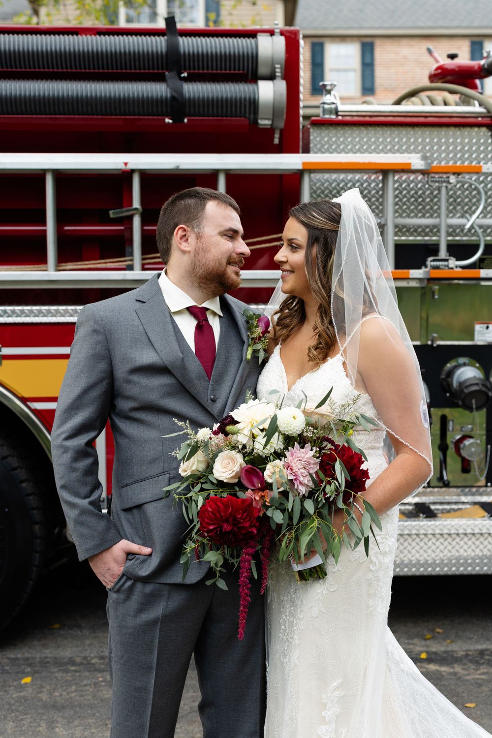 Wedding couple shares a romantic moment next to a fire truck with a beautiful bouquet of flowers.