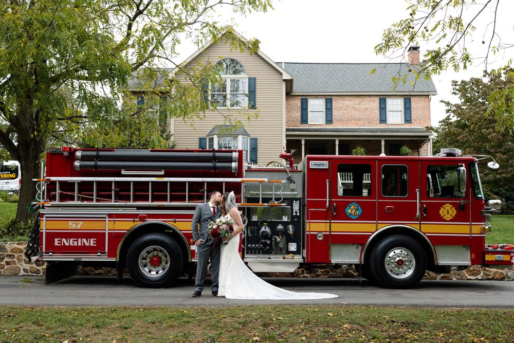Newlyweds pose together in front of a red fire engine on their wedding day.