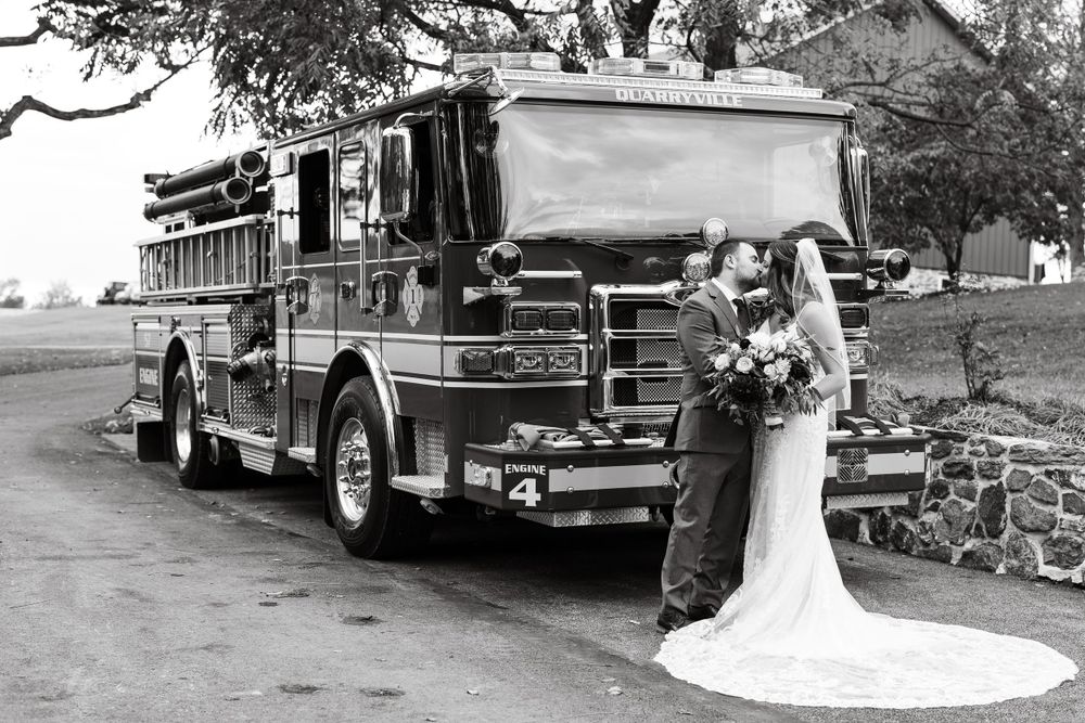 A classic black and white wedding photo features a bride beside a vintage fire truck.