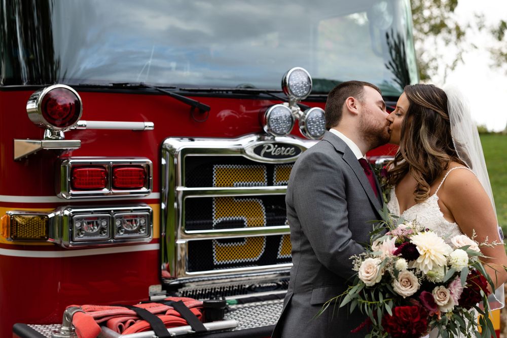 A romantic moment captured between newlyweds in front of a fire engine with floral bouquet.