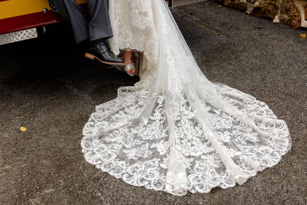 Detailed white lace train of a wedding dress trailing on dark pavement.