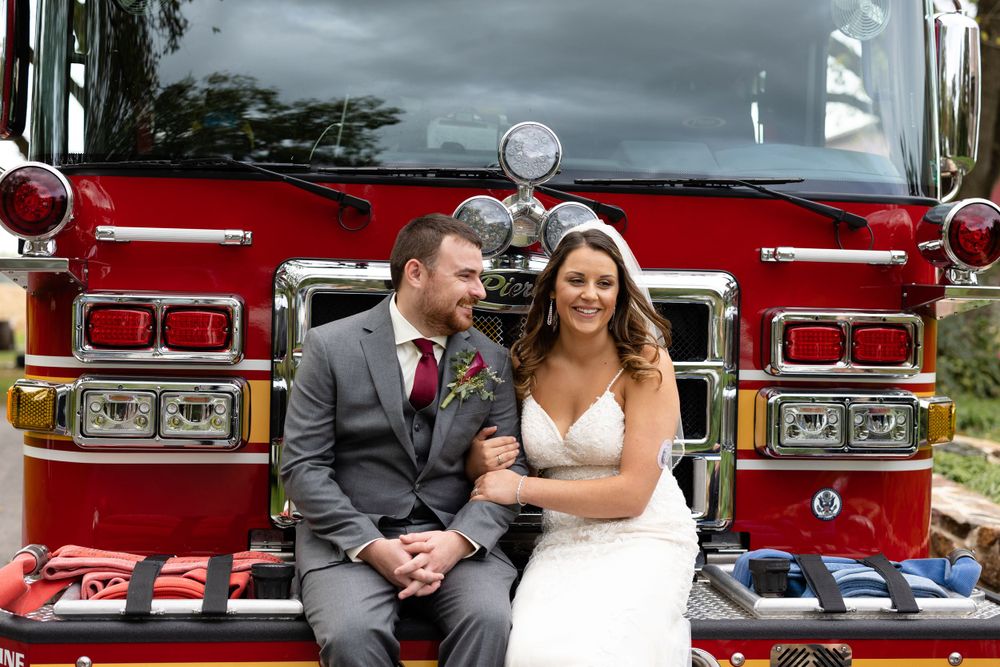 Wedding couple sitting together on the front of a bright red fire truck.