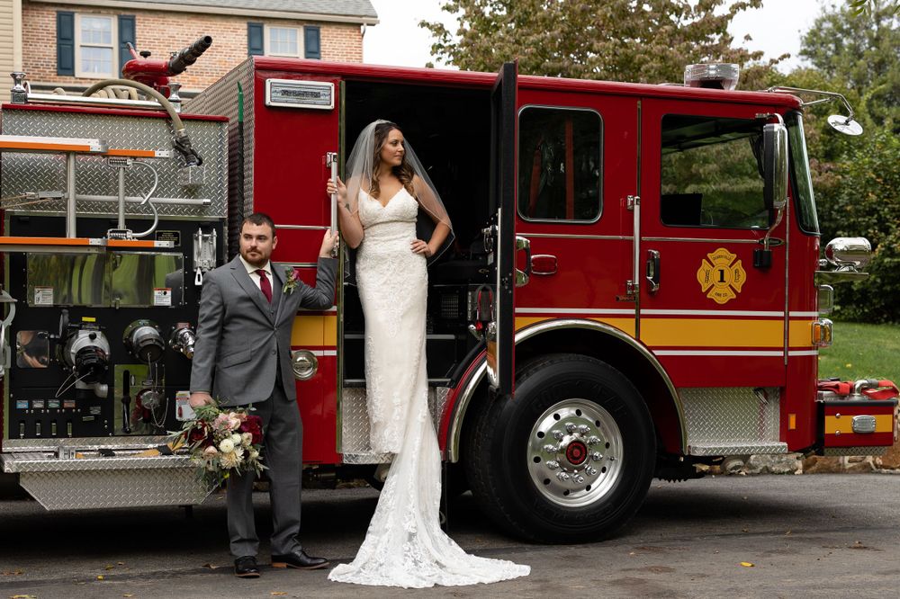 Couple poses with a red fire engine in their wedding attire.
