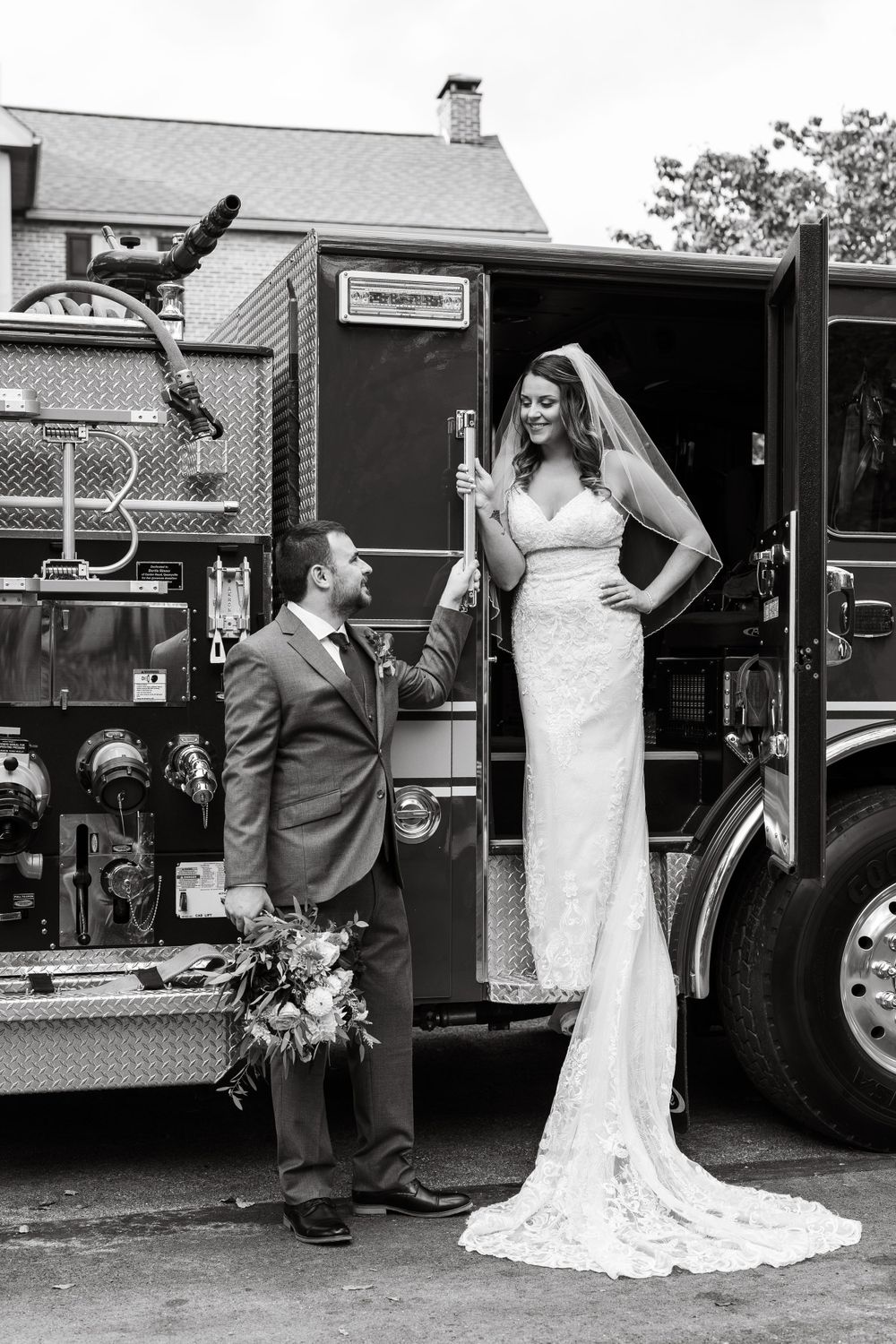 Black and white photo of couple posing with vintage fire truck.