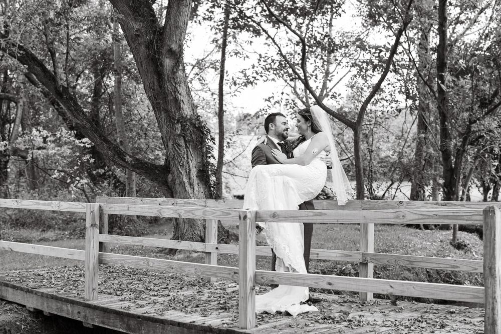 Black and white photo of couple sharing tender moment on wooden bridge.