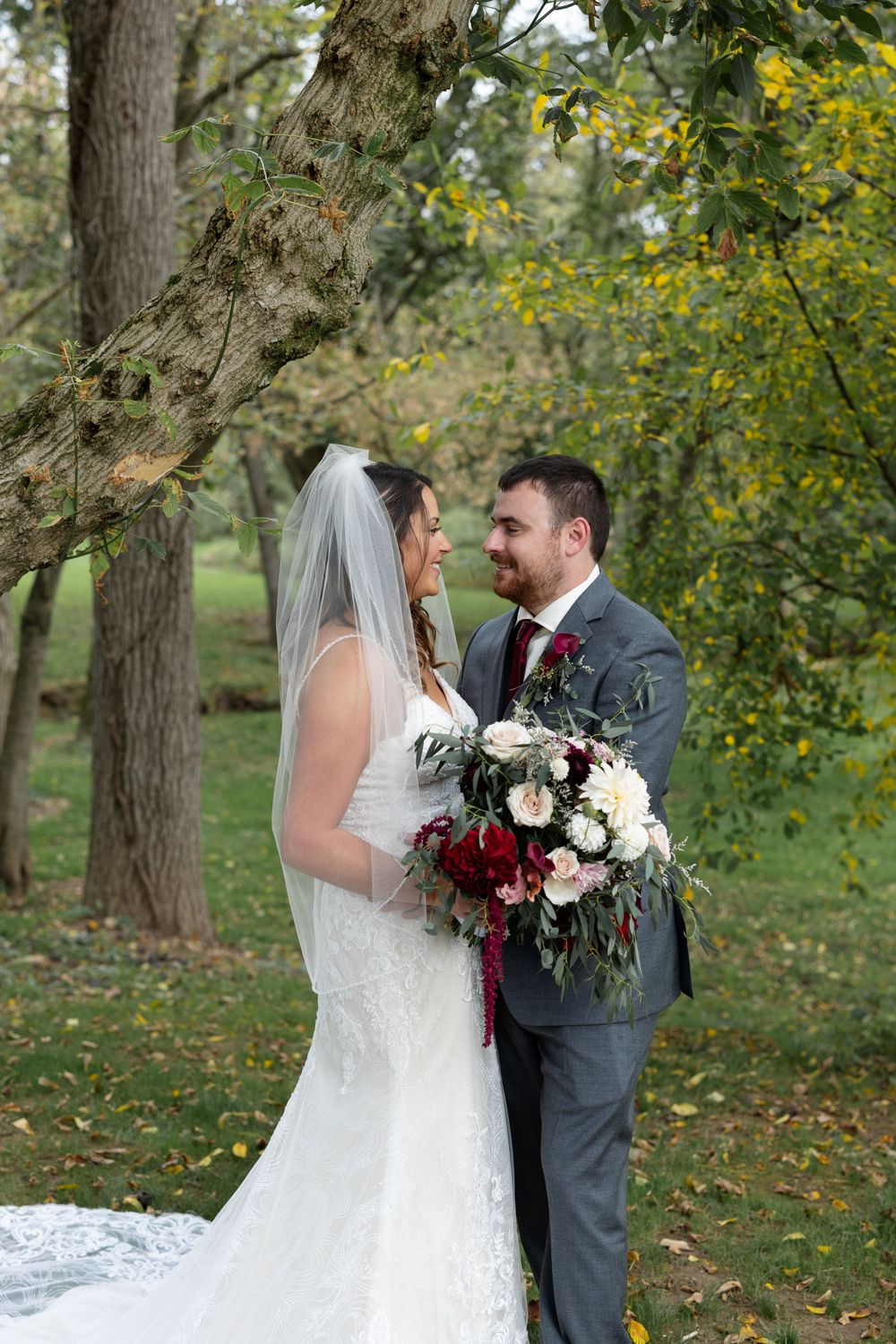 A couple shares an intimate moment during their outdoor wedding photos beneath green and yellow fall foliage.