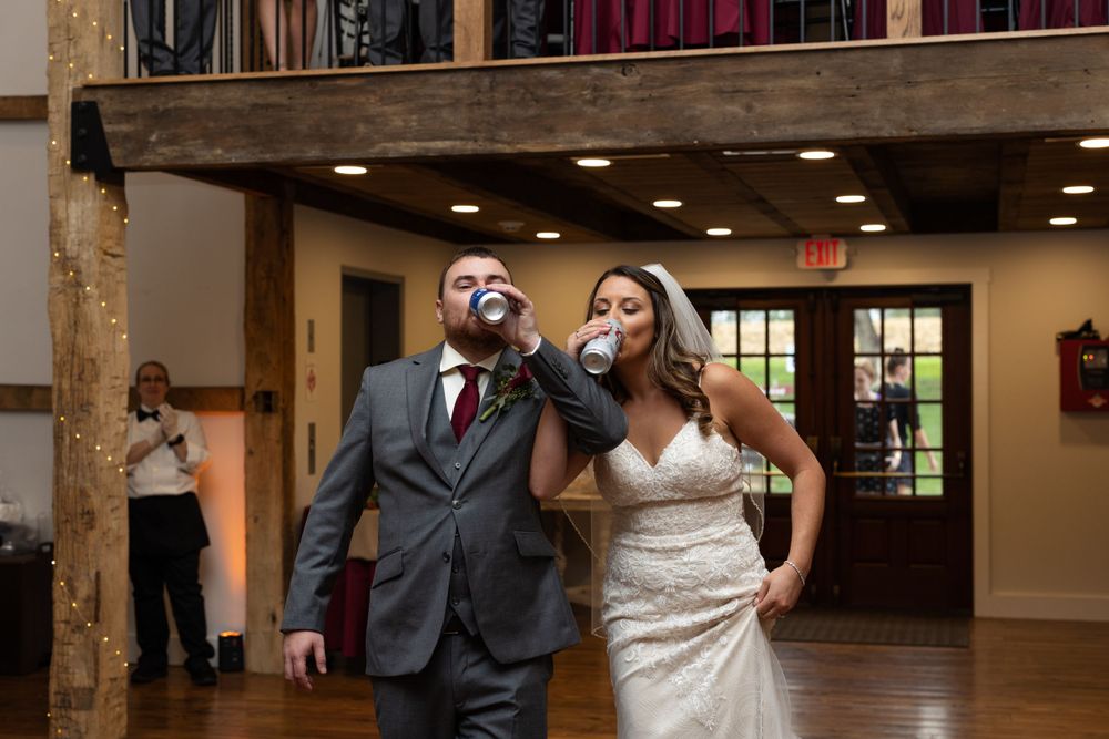 Newlyweds dance and celebrate together in a rustic indoor venue with wooden beams.