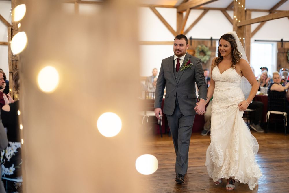 Wedding couple makes their grand entrance into a rustic reception hall with warm glowing lights.