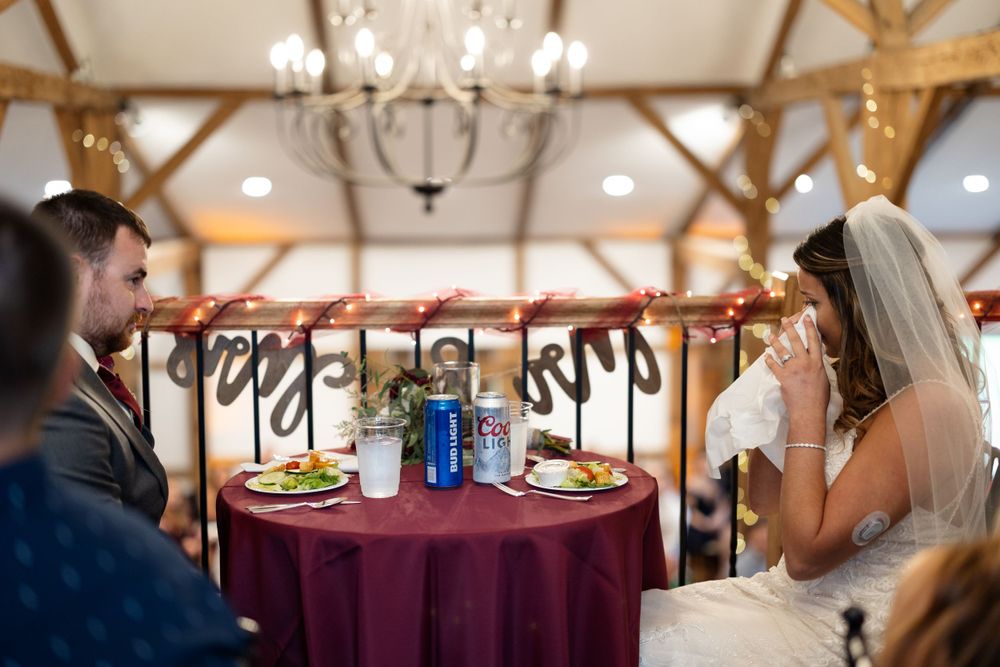 Newlyweds share an intimate moment at their sweetheart table with burgundy linens.