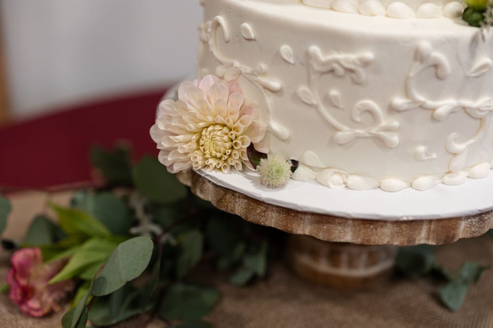 Close-up of a white wedding cake decorated with delicate floral patterns and a pale dahlia flower accent.
