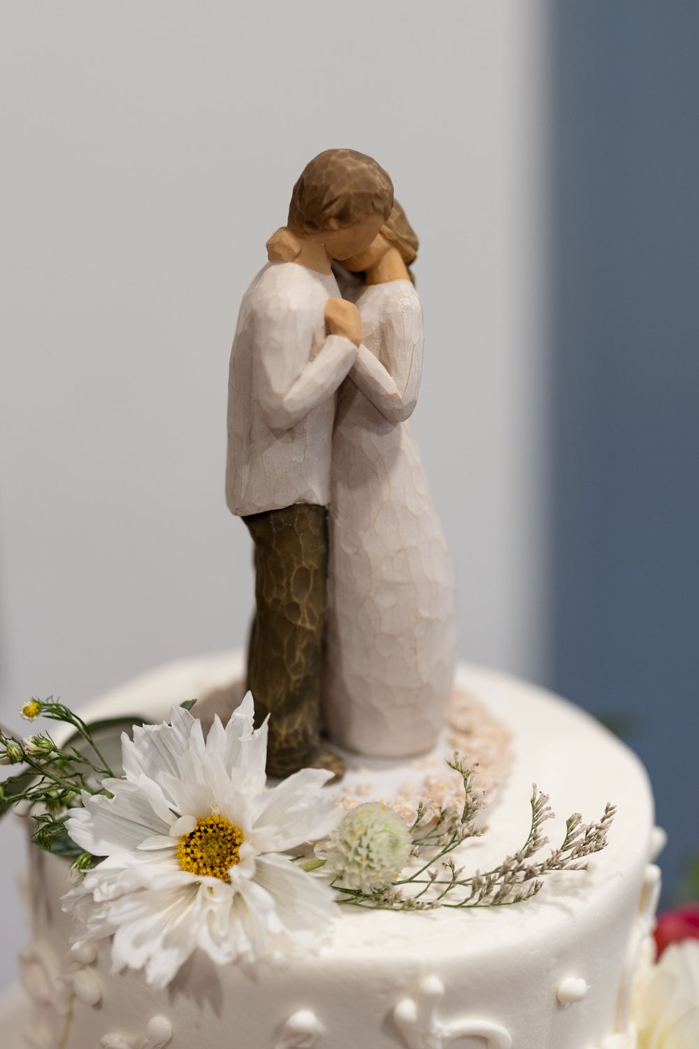 Wedding cake topper featuring a romantic couple figurine with a white daisy decoration on textured frosting.
