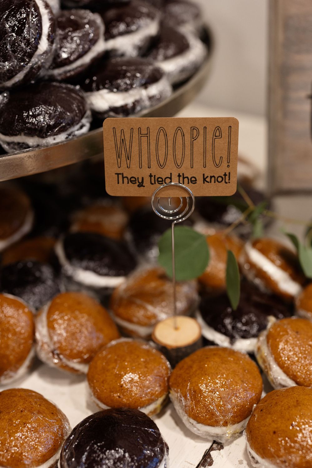 Assorted whoopie pies with wooden sign saying 'WHOOPIE! They tied the knot' at dessert table.