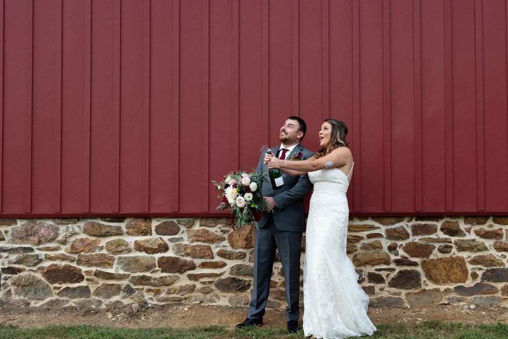 Wedding couple posing against red barn wall with stone foundation.