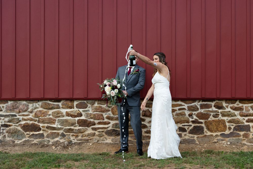 Wedding couple in playful pose against red barn wall.