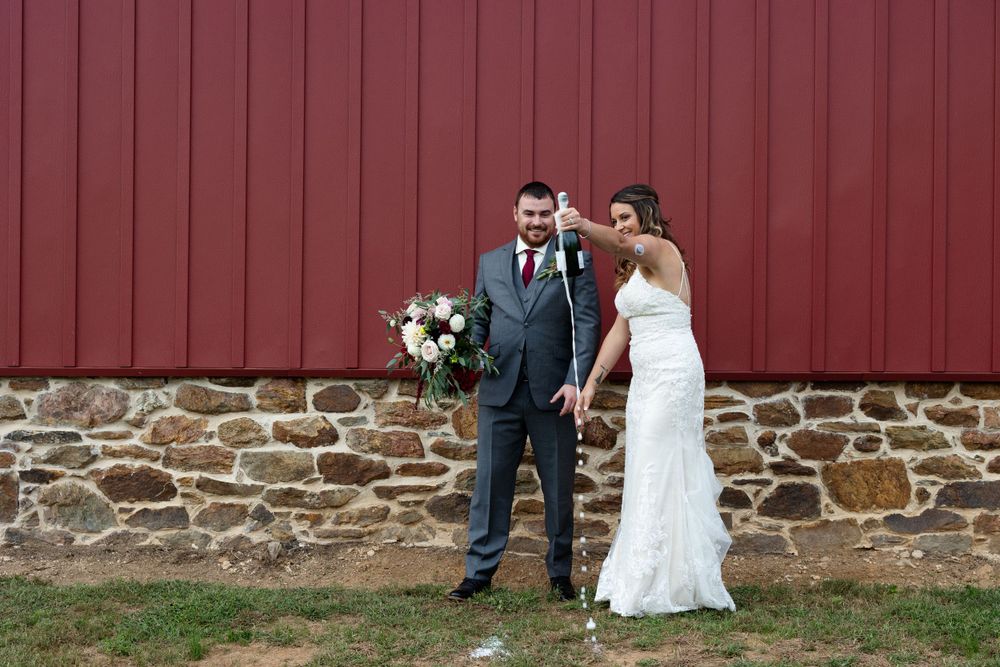 Wedding couple sharing a joyful moment against rustic red barn backdrop.