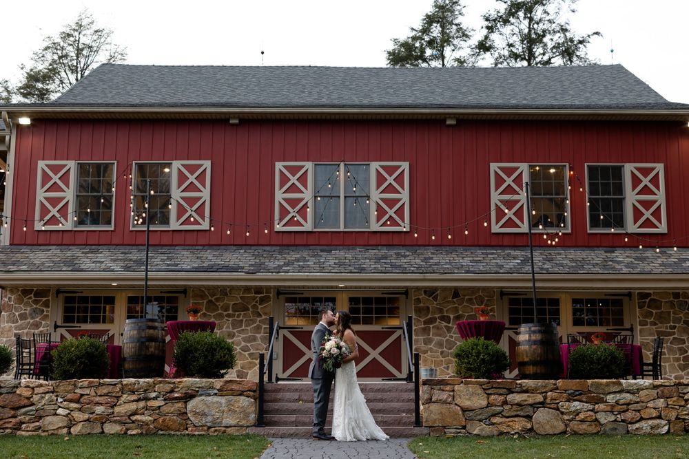 Wedding portrait in front of a charming red barn with classic X-frame windows.