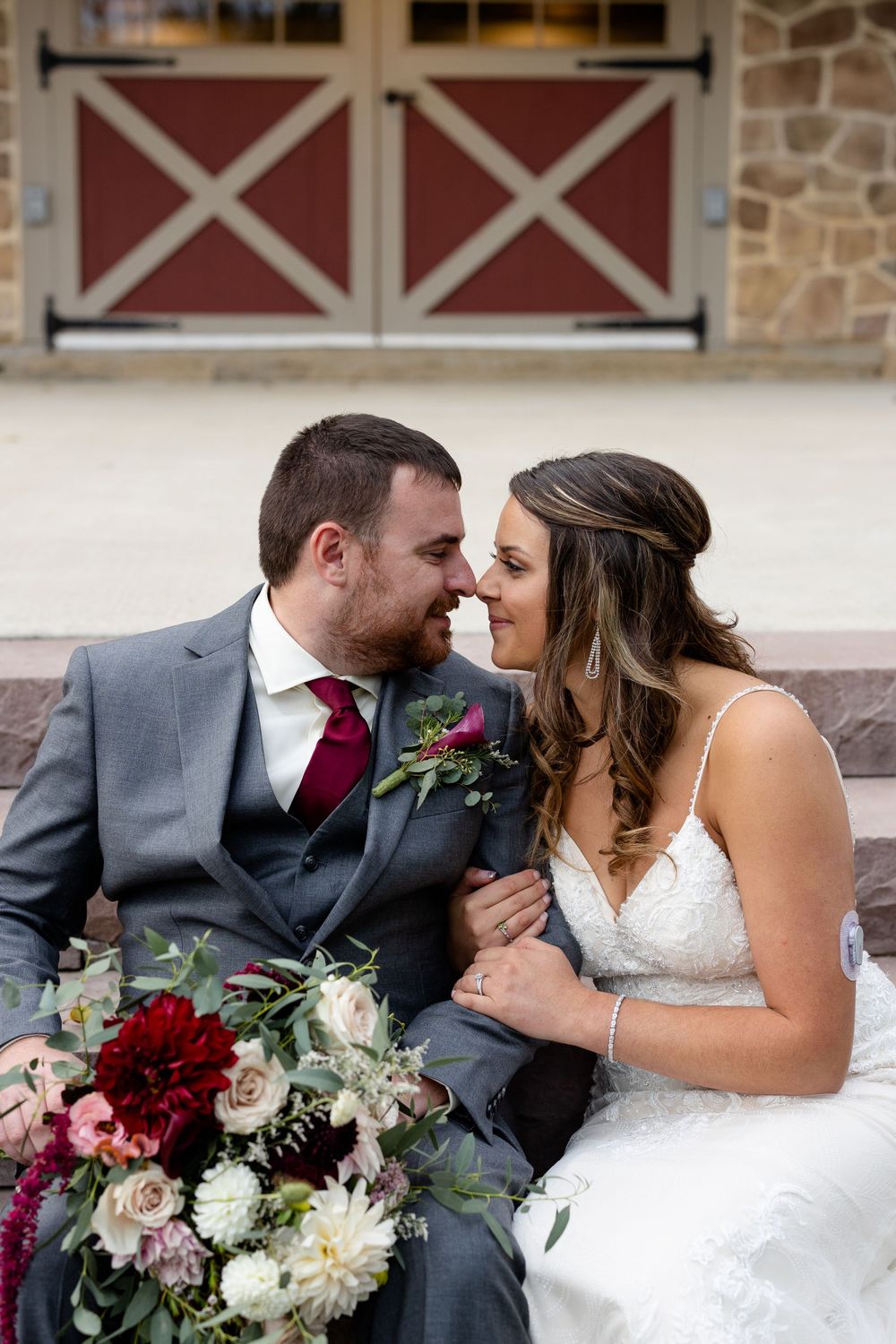 Romantic wedding portrait on steps featuring stunning florals with deep red and white blooms.