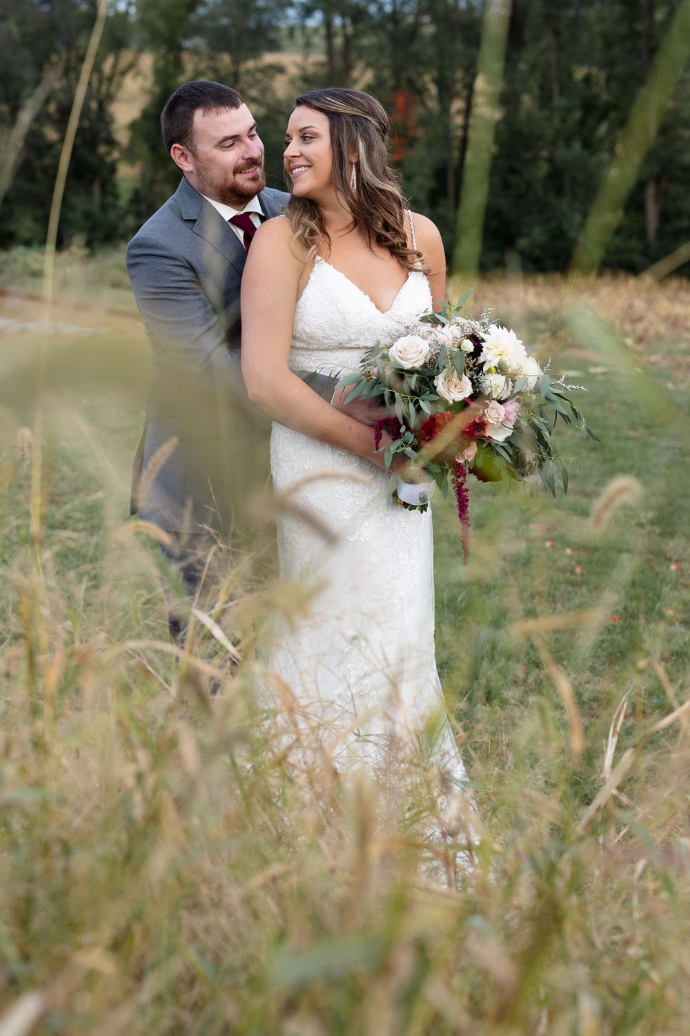 Intimate wedding portrait captured in tall grass with soft natural lighting.