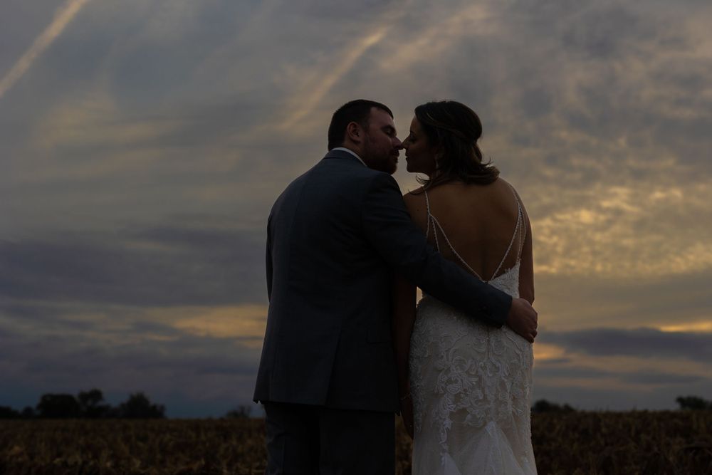 A couple shares an intimate moment at sunset in a rustic field setting during their wedding photoshoot.