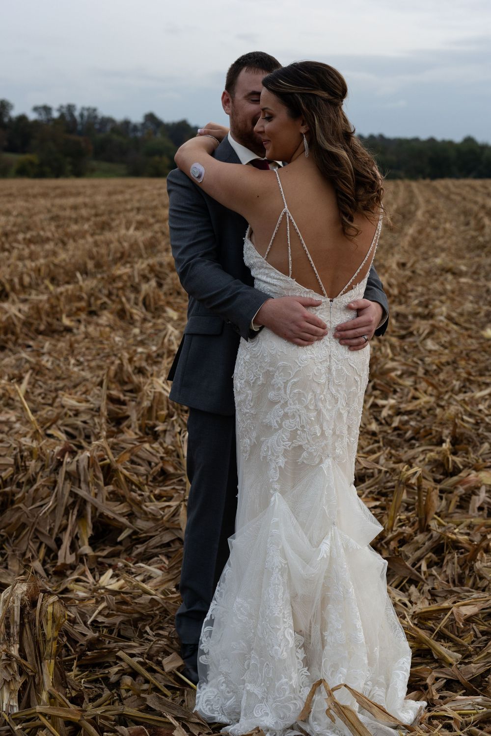 Romantic wedding portrait featuring a detailed lace gown with strappy back design in a harvest field.