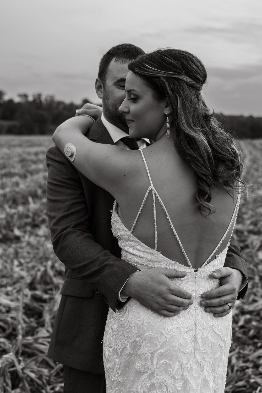 Intimate black and white wedding portrait showcasing a detailed backless dress in a rural setting.