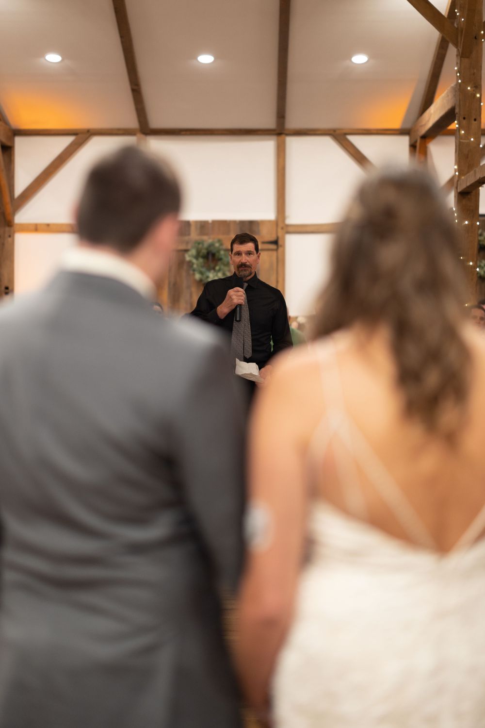 Wedding ceremony in a rustic barn venue with exposed wooden beams and warm lighting.