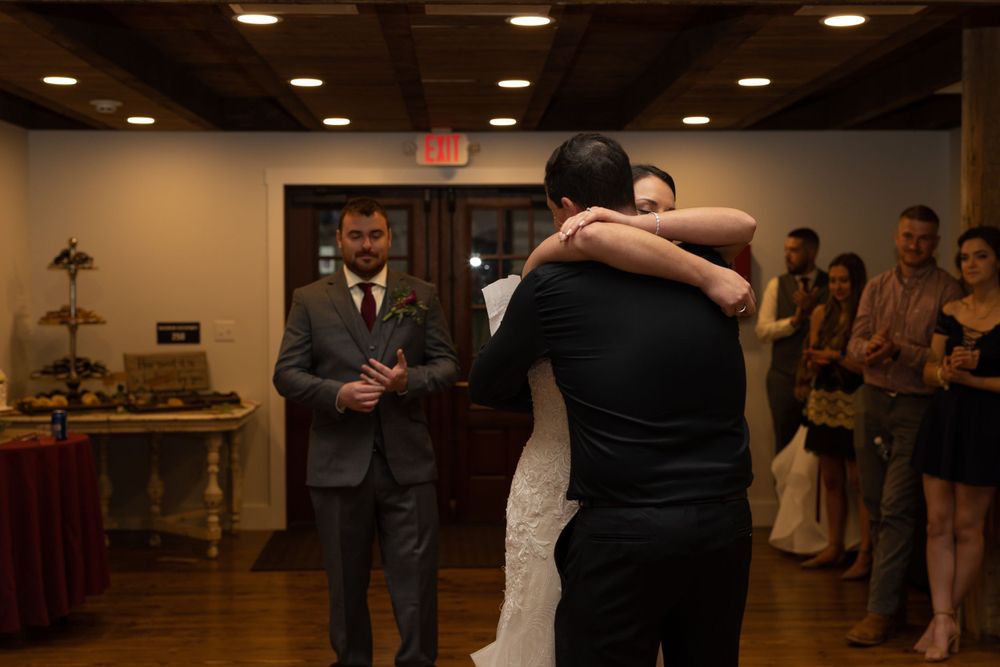 Wedding reception moment captured in a rustic indoor venue with wooden floors and ambient lighting.