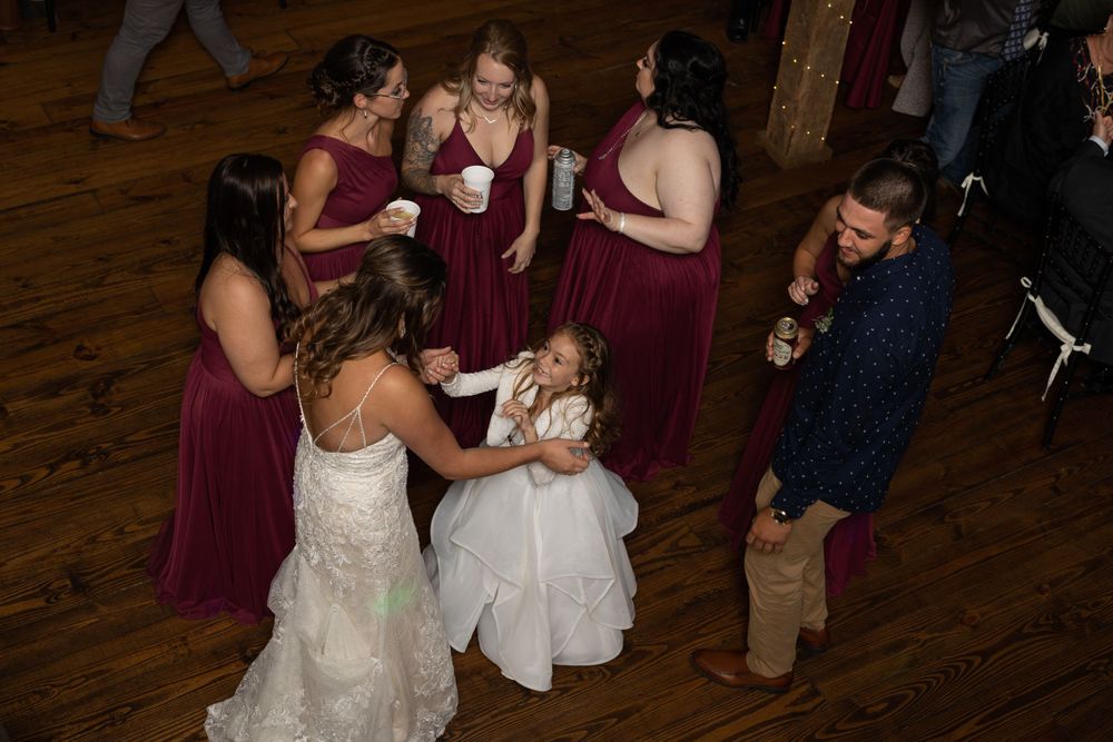 Wedding party in burgundy dresses gathered in a circle during reception festivities.