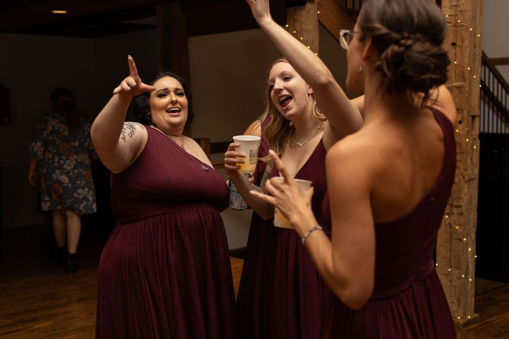 Wedding guests in burgundy dresses laugh and celebrate with drinks on the dance floor.