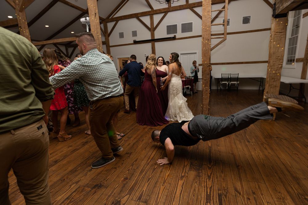 Wedding guests perform energetic dance moves on a rustic wooden dance floor.