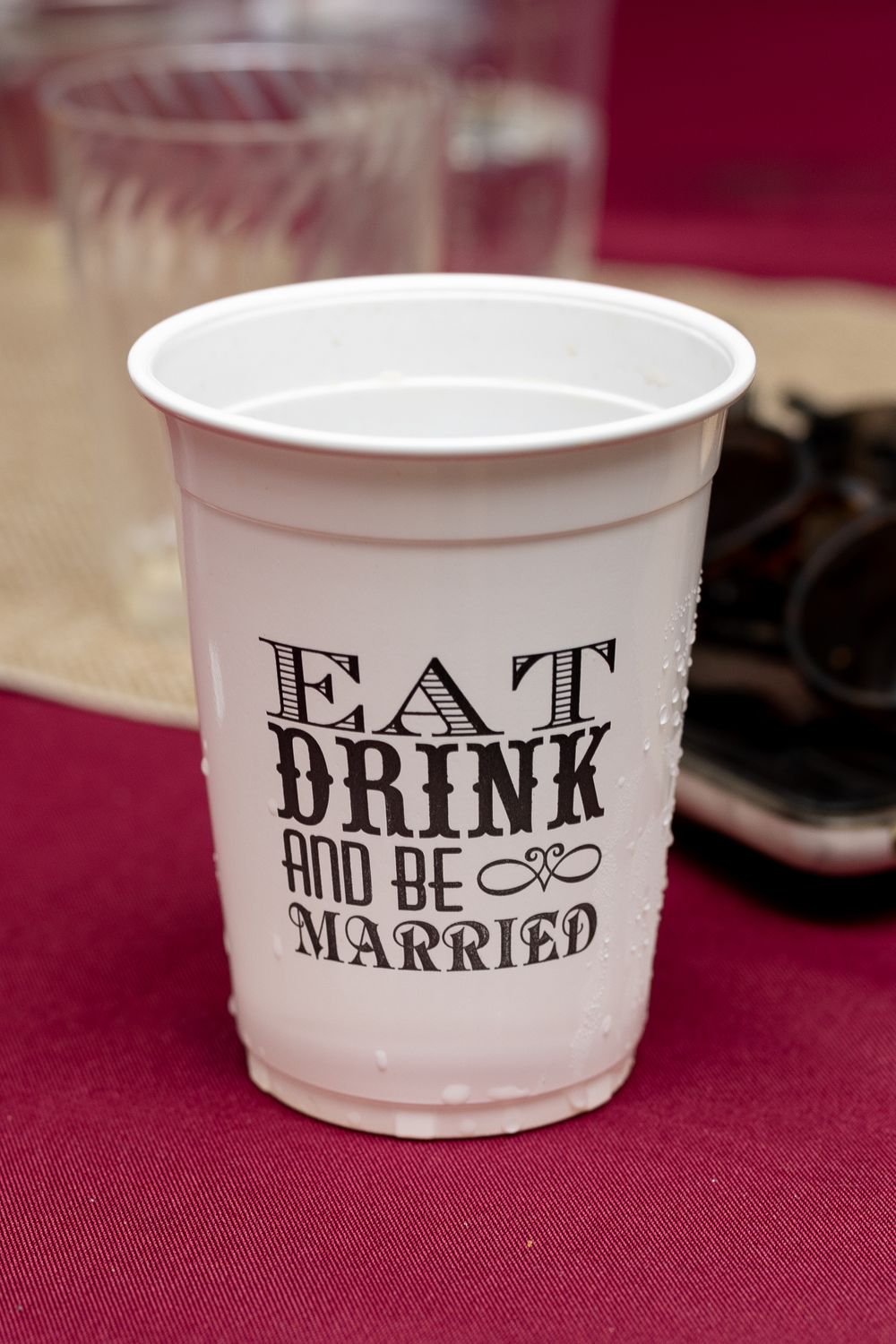 White plastic cup with 'Eat Drink and Be Married' text on burgundy tablecloth.