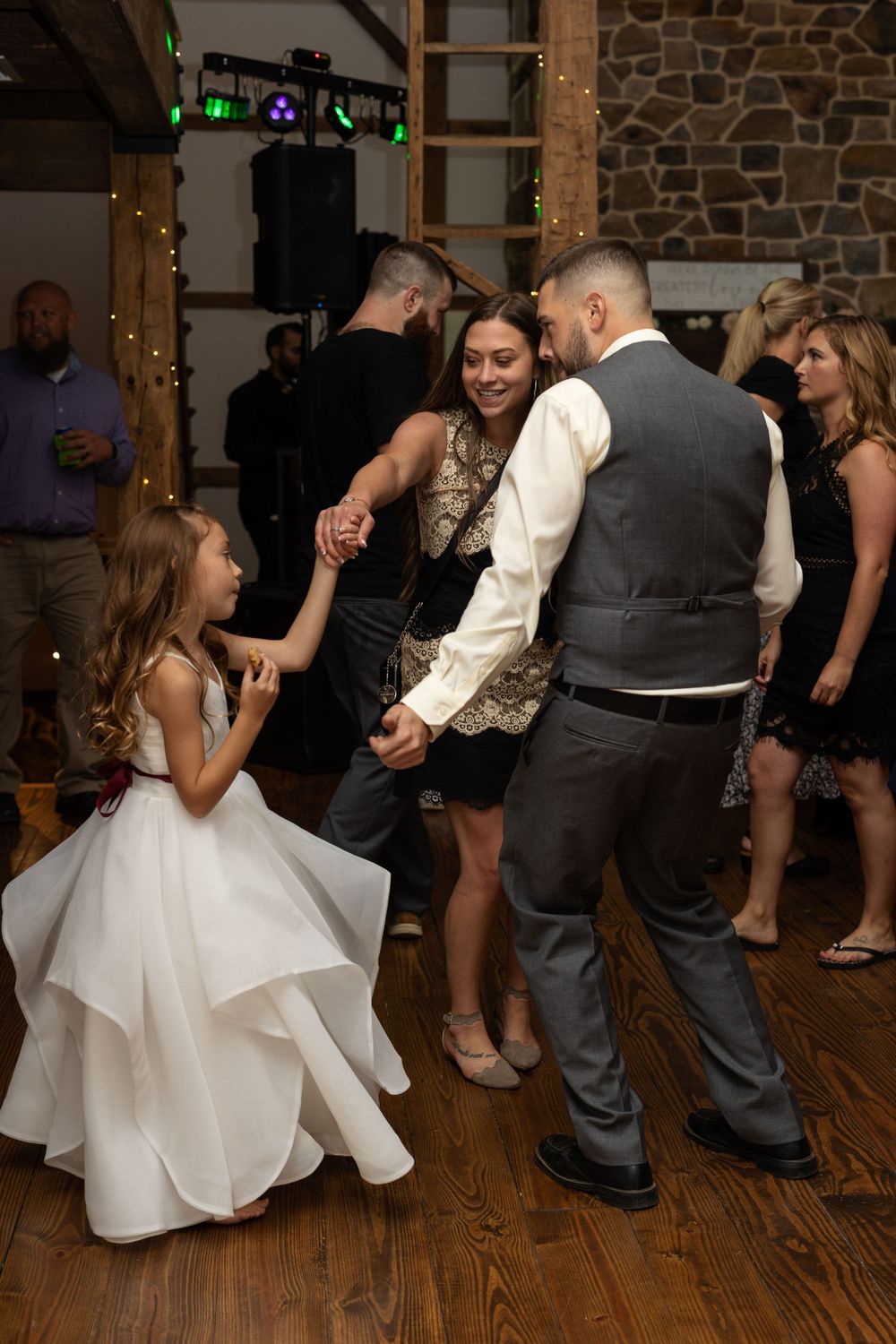 Wedding reception dance party with guests in formal attire on wooden dance floor.
