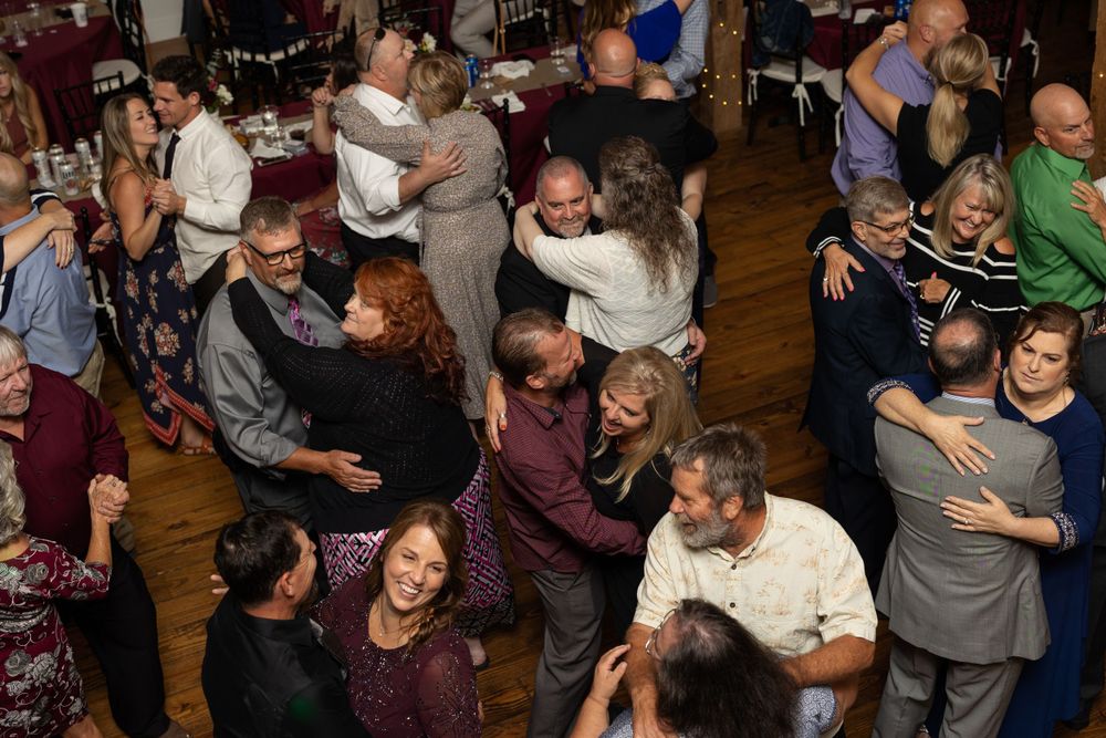 Joyful couples dancing together at a wedding reception in a rustic venue with wooden beams.