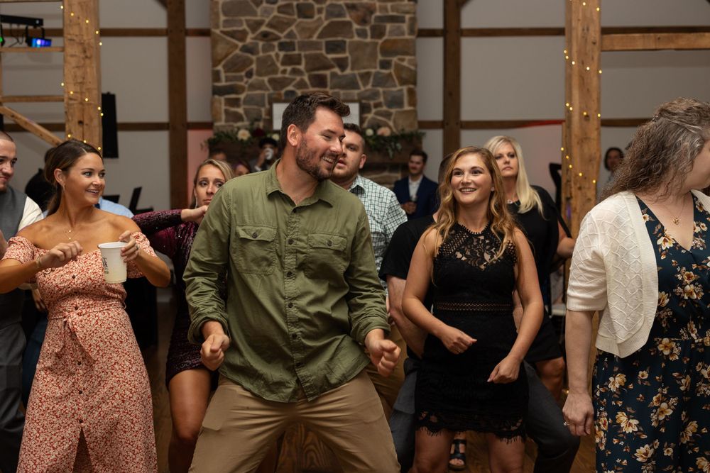 Wedding guests dance enthusiastically on a wooden floor with stone walls and wooden beams in background.