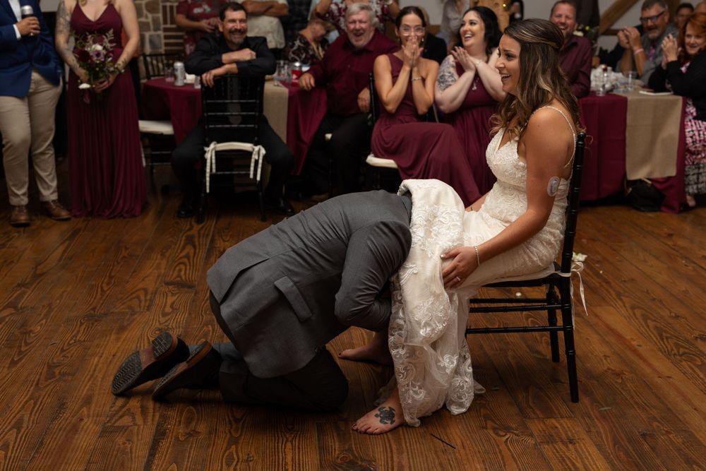 Playful wedding reception moment with participants on a wooden dance floor surrounded by burgundy decorations.