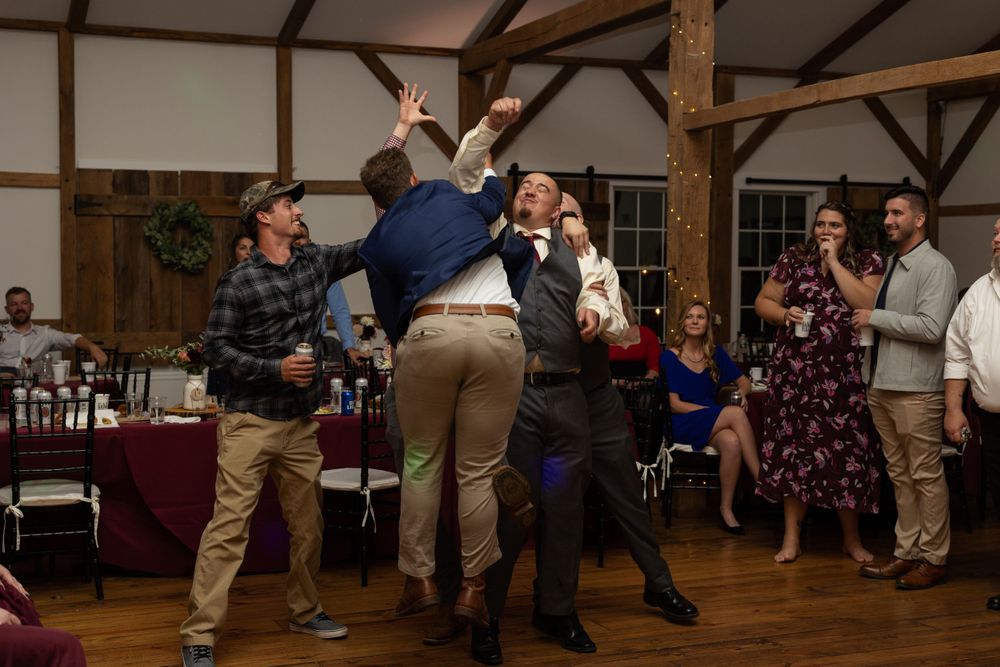 Guests perform an energetic dance move with someone being lifted in the air at a wedding reception.