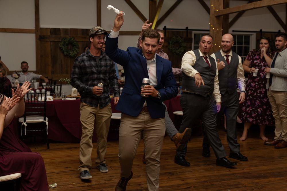 Group of men dancing and celebrating at a wedding reception in a rustic barn venue.