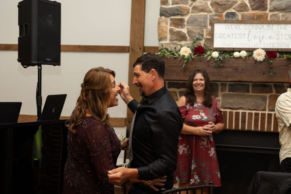 Couple sharing an intimate dance moment at a wedding reception with wood beams and stone fireplace in background.