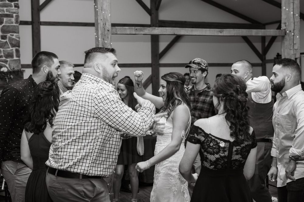 Black and white photo of wedding guests dancing and celebrating in a barn-style reception venue.