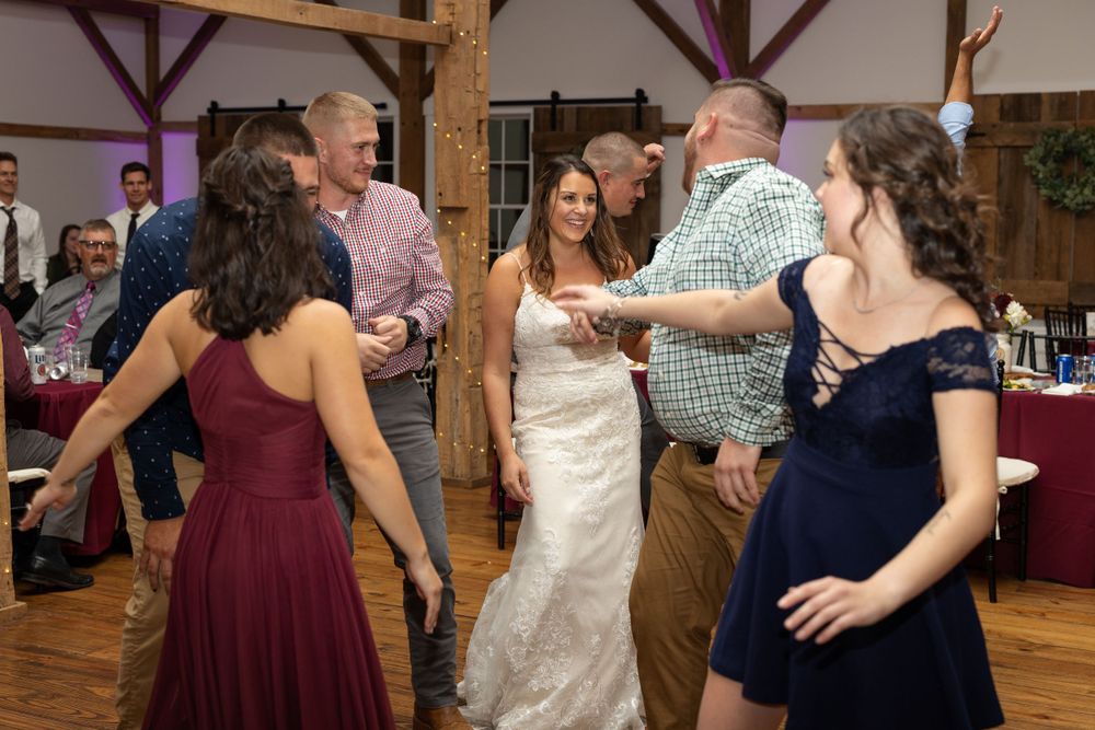 Wedding party dancing together on wooden dance floor during reception celebration.