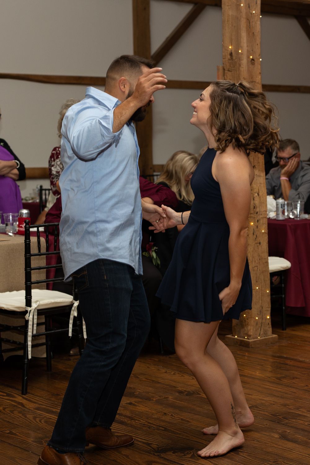 Guests dancing energetically at a wedding reception in a rustic venue with wooden beams.