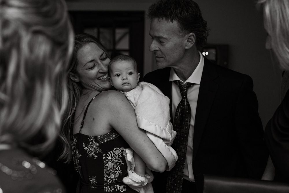 Black and white candid moment of family with baby at formal event.