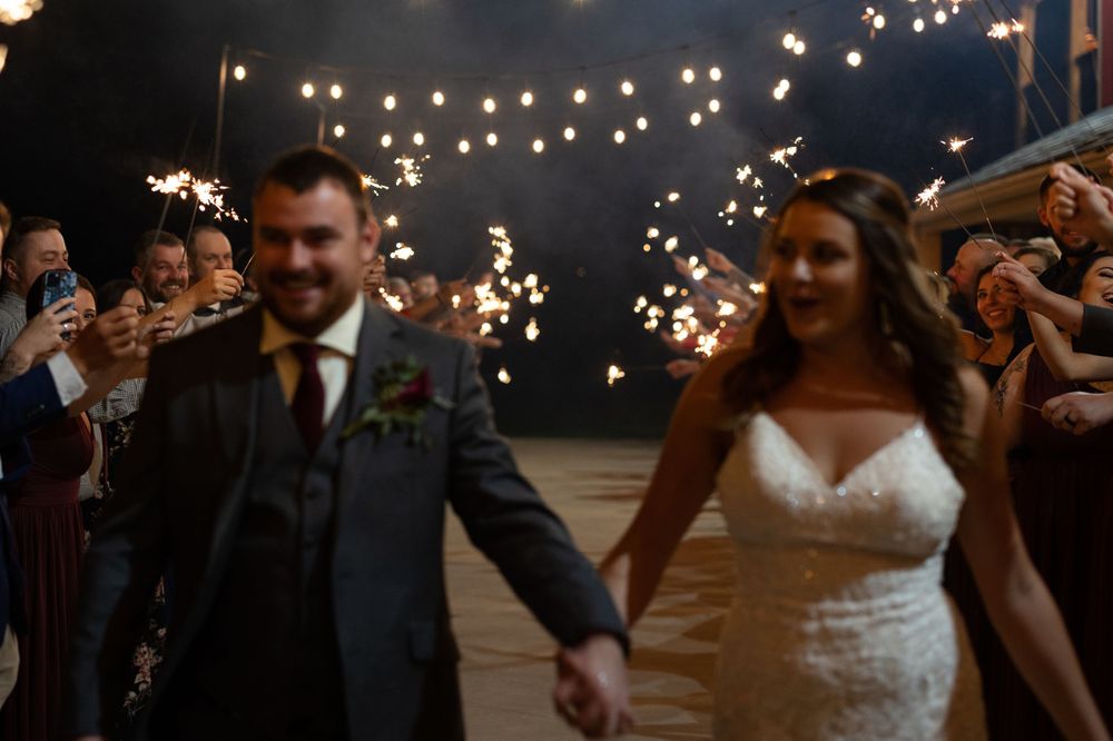 Newlyweds walking through sparkler exit during nighttime wedding celebration.