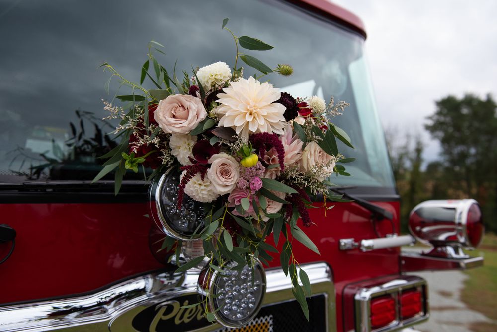 Wedding bouquet with blush and burgundy flowers rests on vintage red fire truck.