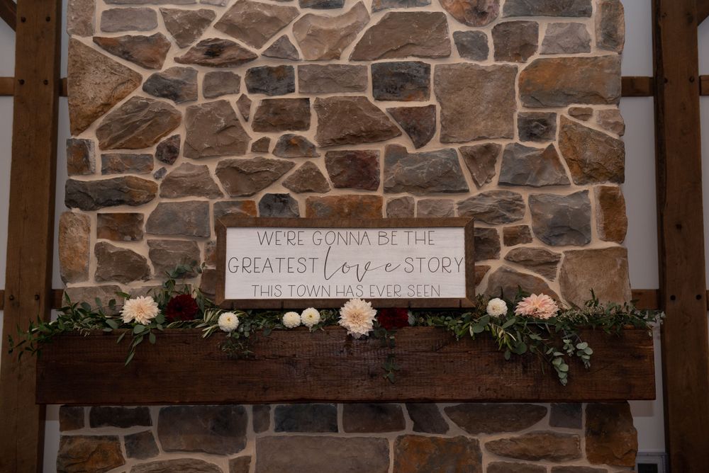 Rustic wedding signage mounted on stone wall with floral decorations.
