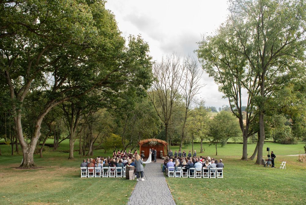 Wedding ceremony setup with stone pathway leading to wooden arch surrounded by trees.