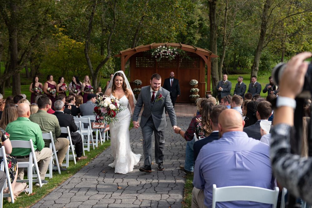Wedding ceremony recessional on stone pathway with guests seated on white chairs.