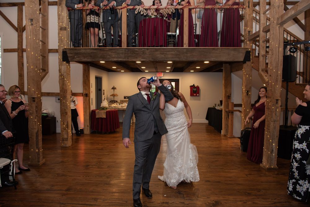Couple dancing in rustic barn venue with wooden beams and balcony.